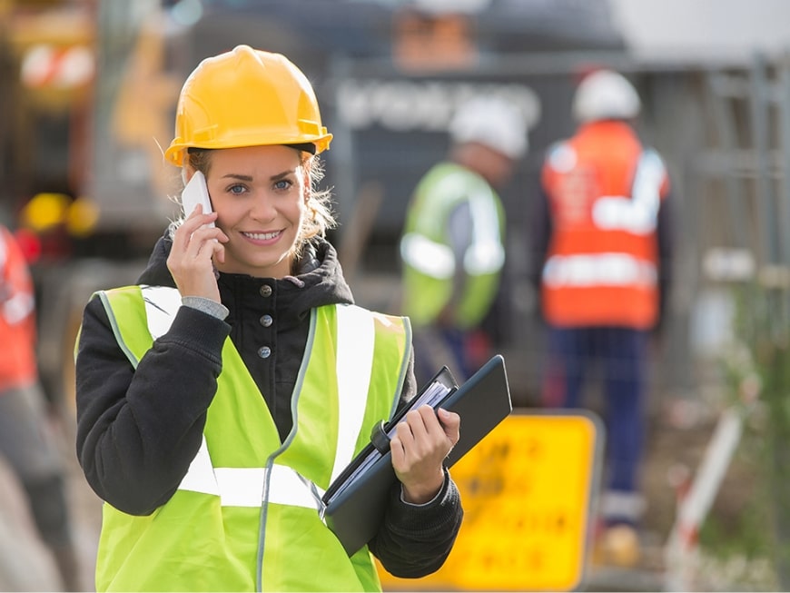 Female construction worker with safety gear and clipboard on the phone